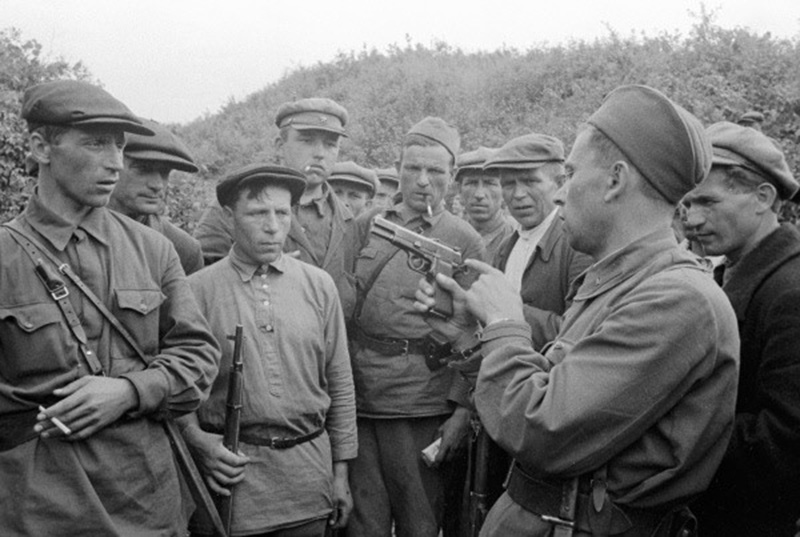 Командир партизанского отряда знакомит бойцов с трофейным оружием