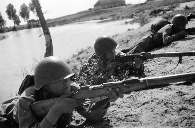 Красноармейцы с винтовками Мосина занимают огневую позицию после переправы через реку.